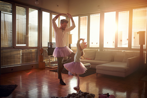 A young Dad and his little daughter practicing ballet moves while they have a training in a playful atmosphere at home together. Family, together, home