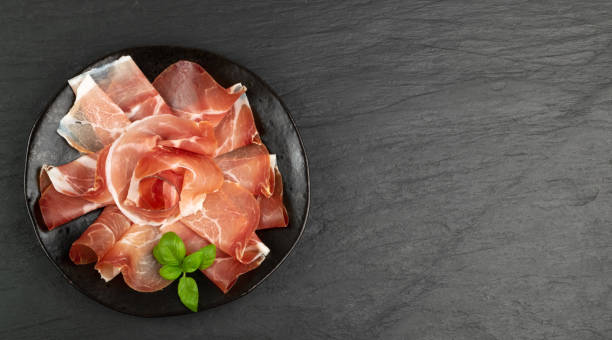 Slices of Prosciutto, Spanish Jamon Cut, Parma Ham Slices of prosciutto on black plate top view with copy space. Spanish jamon cut, parma ham, serrano or iberico on black background prosciutto stock pictures, royalty-free photos & images