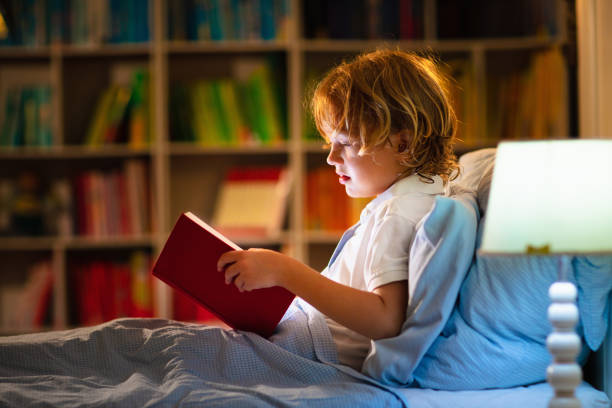istock Child reading book in bed. Kids read at night. 1320649183