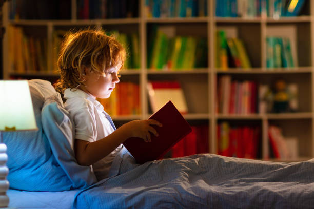 istock Child reading book in bed. Kids read at night. 1320649208