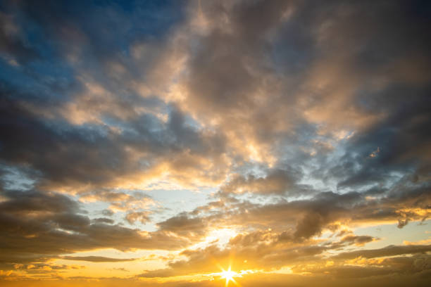 istock Dramatic sunset landscape with puffy clouds lit by orange setting sun and blue sky. 1320652660