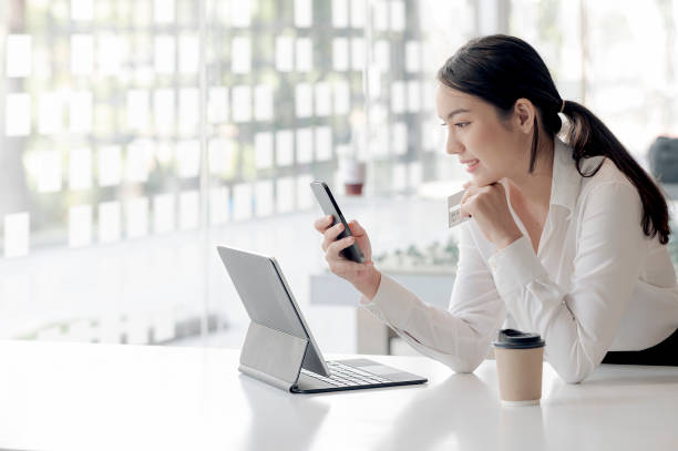 Beautiful businesswoman using smartphone shopping online. Portrait of young asian woman holding smartphone and credit card while sitting at office desk. demanding photos stock pictures, royalty-free photos & images