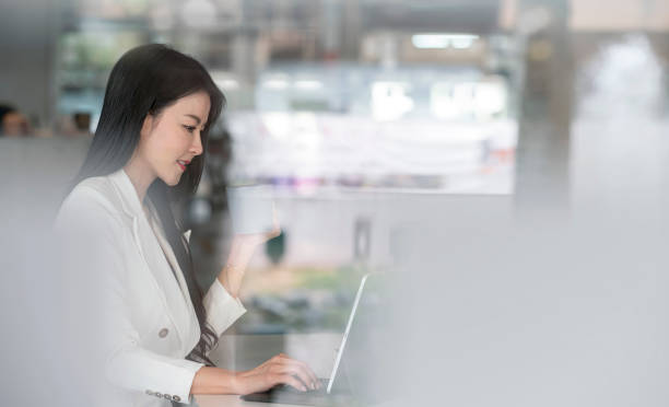 istock businesswoman holding mug and working on laptop computer while sitting in modern office. 1320658316