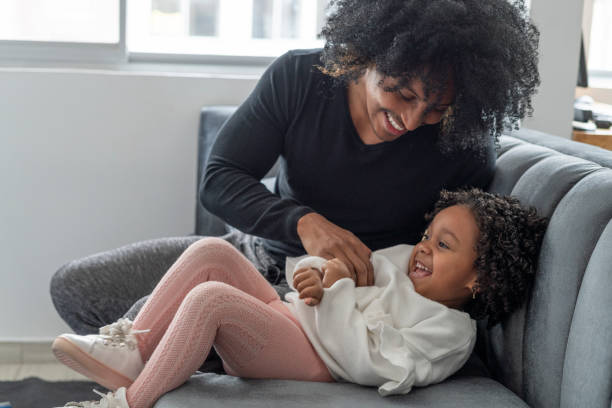 istock Young black father with his Latin daughter both sitting playing on the couch on a beautiful day while isolated from COVID 1320658336