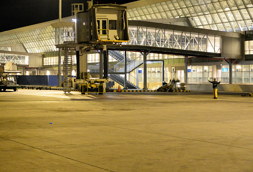 Addis Ababa, Ethiopia: an aircraft marshaller prepares the arrival of a flight at a passenger boarding bridge - air-side of Terminal 2, apron at night - Addis Ababa Bole International Airport (IATA: ADD, ICAO: HAAB).