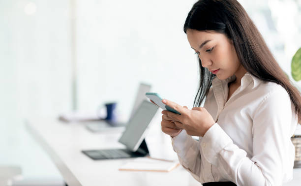 istock Young asian woman using smartphone while standing in office. 1320658491