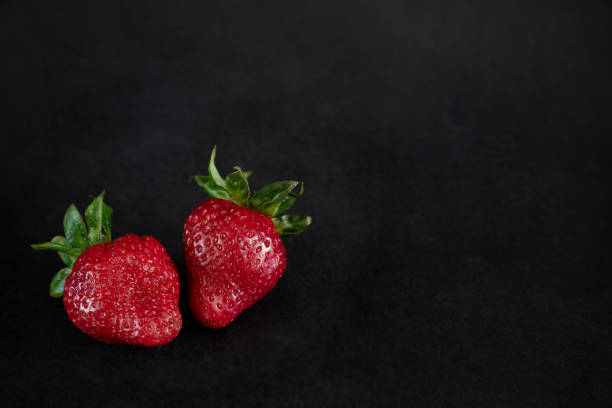 istock Two ripe red strawberries on black background 1320659329