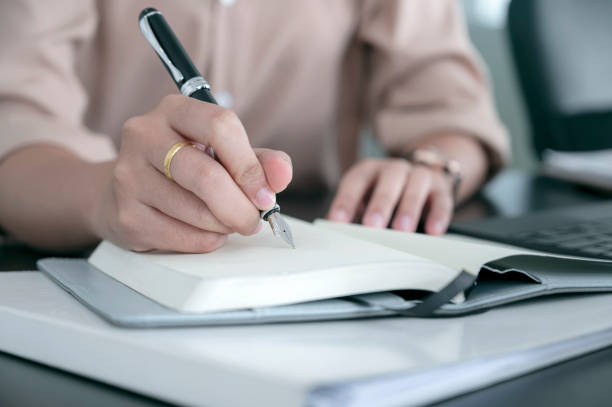 istock Closeup female hand writing on diary with pen. 1320659497