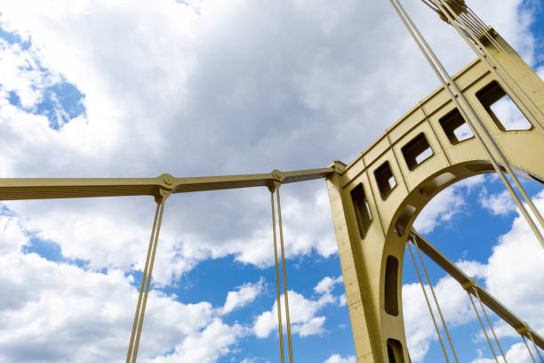 istock Yellow suspension bridge structure against a bright blue sky with white clouds 1320659587