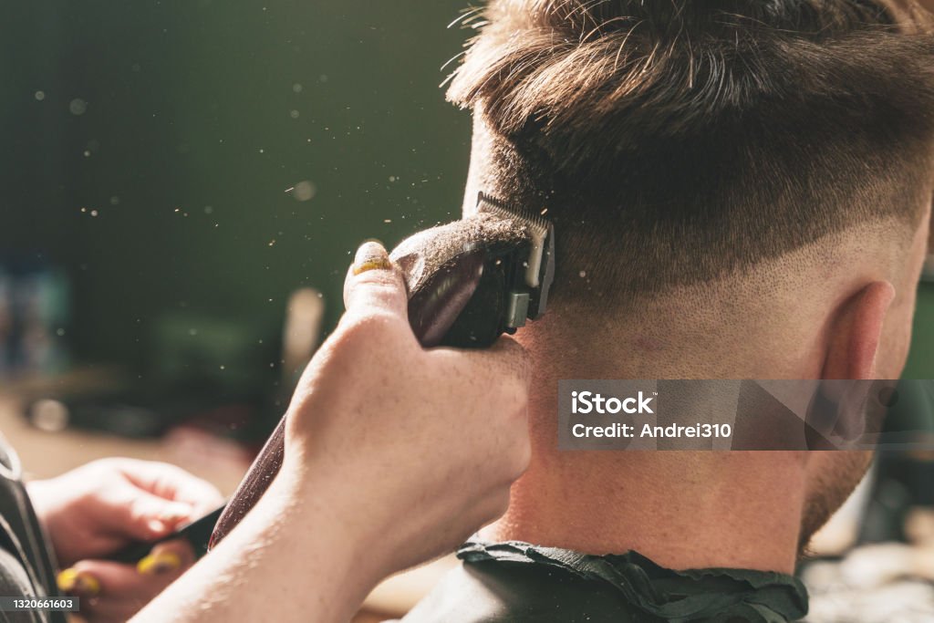 Mädchen Friseur macht einen Haarschnitt zu einem jungen Kerl mit einem Haarschneider in einem Friseurladen - Lizenzfrei Haare schneiden Stock-Foto