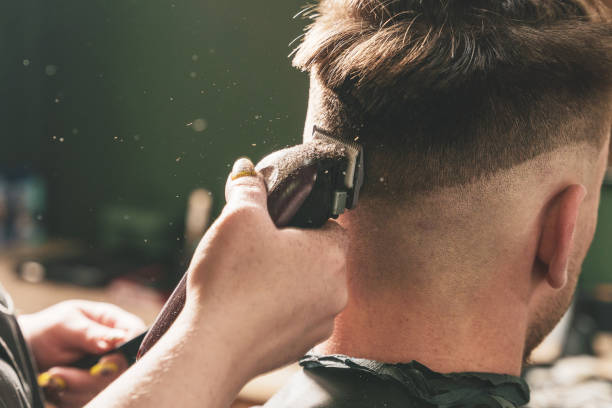 chica peluquera hace un corte de pelo a un chico joven usando una cortadora de pelo en una barbería - barbero peluquero fotografías e imágenes de stock