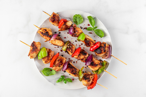 Chicken breast fillet grilled barbecue skewers with vegetables and basil in a plate on white table. top view. tasty food