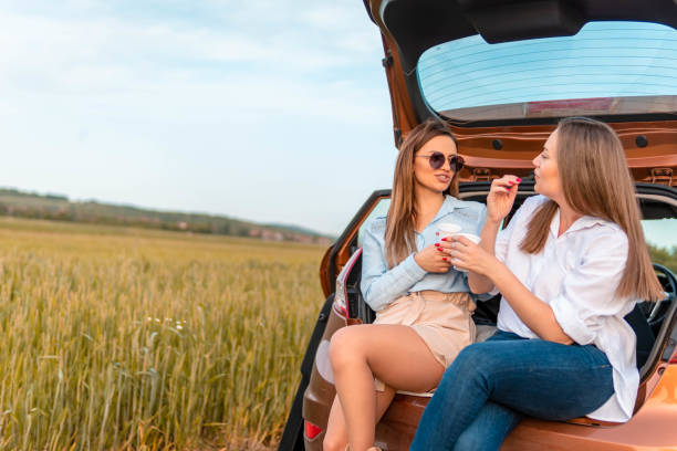 istock Smiling young women sitting in open car trunk and relaxing while taking a break from a road trip. 1320663095