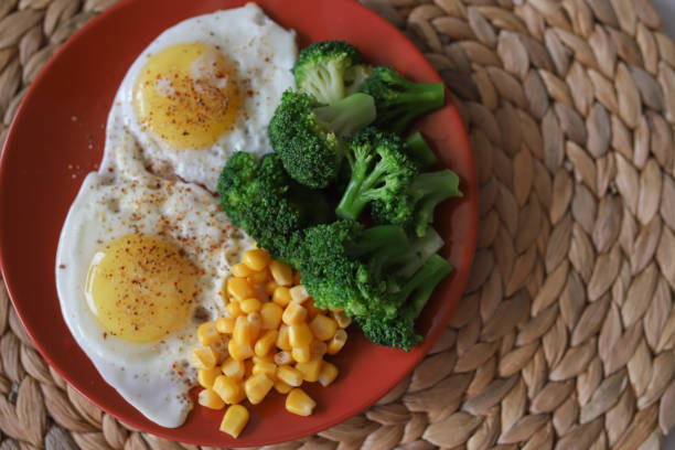 Two fried eggs are sprinkled with pepper, with green broccoli and canned cuckoo. View from above.