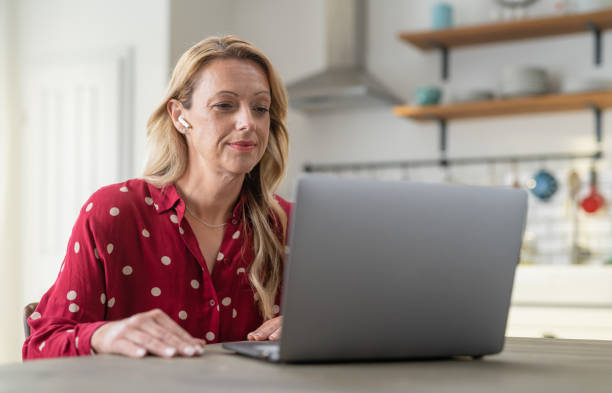 istock Beautiful Woman Smiling And Using Laptop While Sitting In Her Kitchen 1320668610