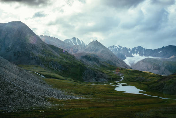 istock Atmospheric alpine landscape with sharp pinnacle under cloudy sky. Big glacier and mountain lake in green valley. Awesome highland scenery with beautiful glacial lake and sunlight on hills and rocks. 1320669782