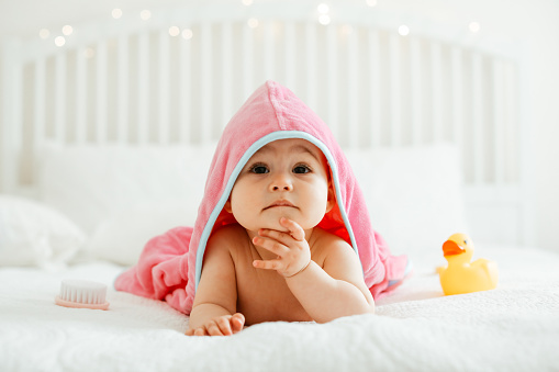 Cute baby girl or boy after shower with towel on head in white sunny bedroom. Child  relaxing in bed after bath