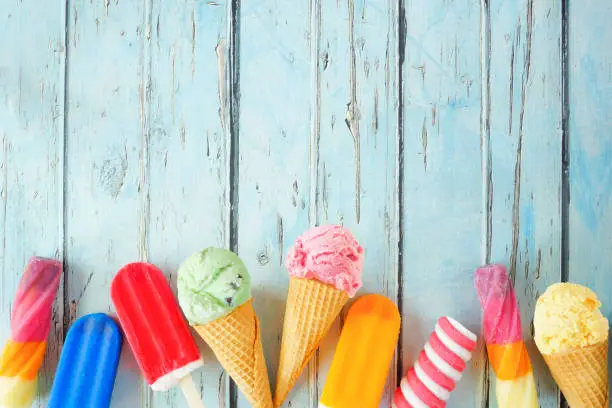 Photo of Variety of colorful summer frozen desserts. Bottom border on a rustic blue wood background.