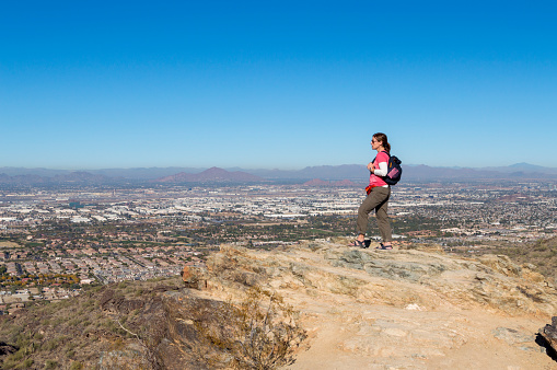 This woman is enjoying a hike through the desert terrain on the Mormon Trail.  This hike is located on South Mountain Park in Phoenix, Arizona and enjoys expansive views and rugged terrain.  In this shot, the woman is viewing the Phoenix skyline below.