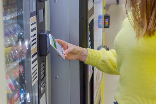mujer que paga en la máquina expendedora usando el teléfono inteligente - vending machine fotos fotografías e imágenes de stock