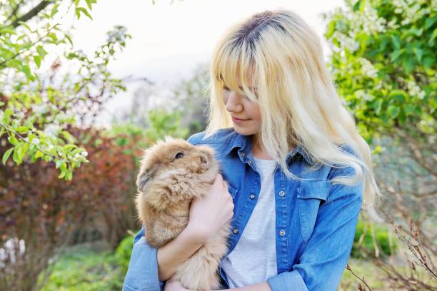 istock Young blonde woman with decorative rabbit in the spring garden 1320688052