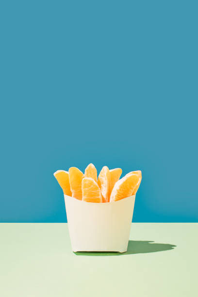 kreative gesunde ernährung idee, frische orange scheiben in fast food pommes frites tasche auf hellblauem und grünem hintergrund. modernes minimalistisches sommerkonzept, vertikale kopierraumanordnung. - french fries fast food french fries raw raw potato stock-fotos und bilder