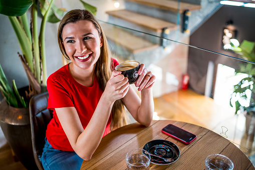 Young smiling woman sitting in cafe and drinking coffee