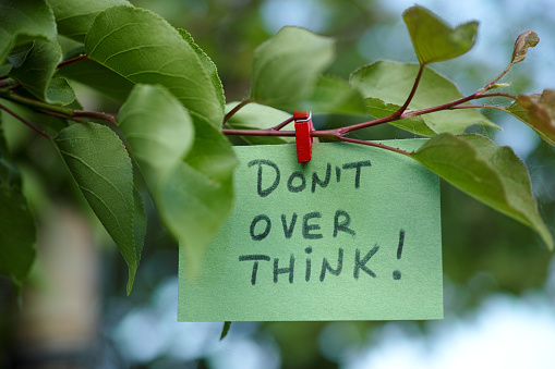 A paper note with the phrase Don't over think written on it hanging on a tree. Close up. Concept image.