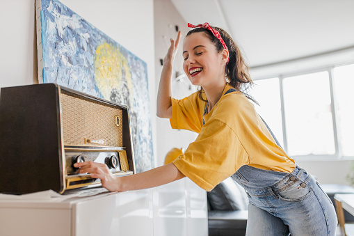 Woman having fun, singing, dancing and listening music at home