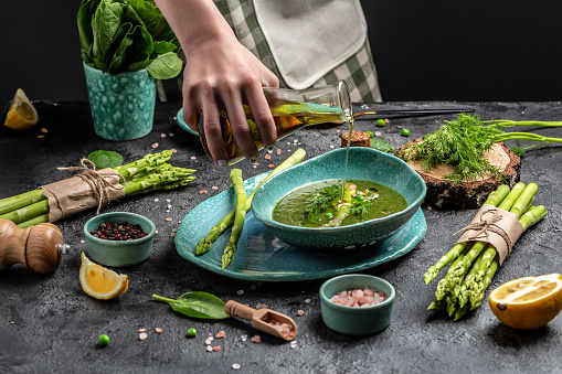 Spring detox Asparagus green cream soup in bowls. Cook hand sprinkling olive oil. Clean eating, dieting, vegan, vegetarian, healthy food concept.