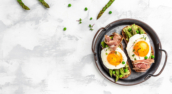 toasts with avocado, asparagus, jamon, ham, prosciutto and fried egg, Breakfast. Long banner format, top view