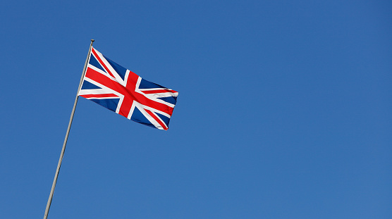 The British flag is waving on a flagpole against a clear blue sky.