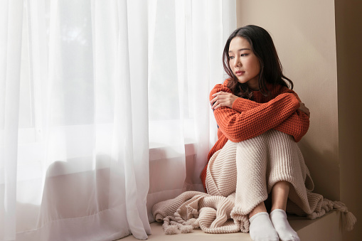 A beautiful Asian woman. young women the pensive face looking away thinking of problems sit alone at home, Sad eyes, Winter sadness