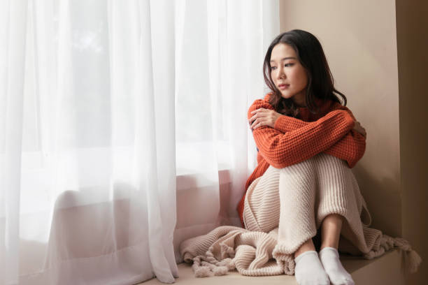 A beautiful Asian woman. young women the pensive face looking away thinking of problems sit alone at home, Sad eyes, Winter sadness stock photo