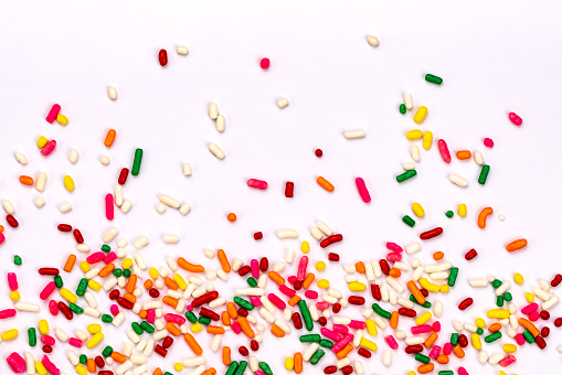 Top view of multicolor rainbow sprinkles scatter on white background.
