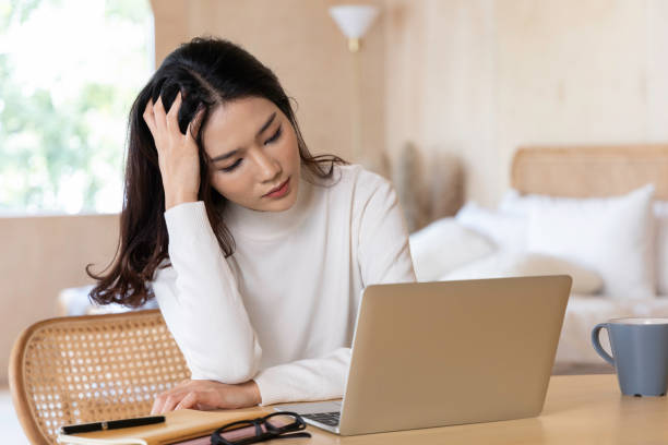 Portrait of a beautiful young Asian woman work from home. She was suffering from stress from reading content on the Internet. She follows the news of the coronavirus outbreak. stock photo