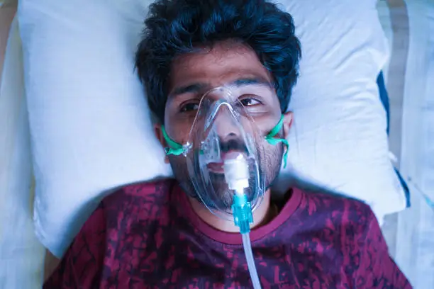 Top View of young man breathing on ventilator or oxygen concentrator mask at hospital due coronavirus covid-19 dyspnea or shortness of breath - Concept of covid viral infection millennial people