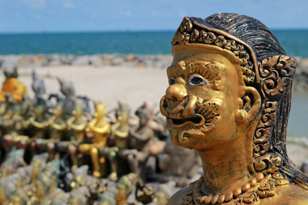 Face of a gold Buddhist statue at a shrine in southeast Asia with beach and ocean blurred in the background