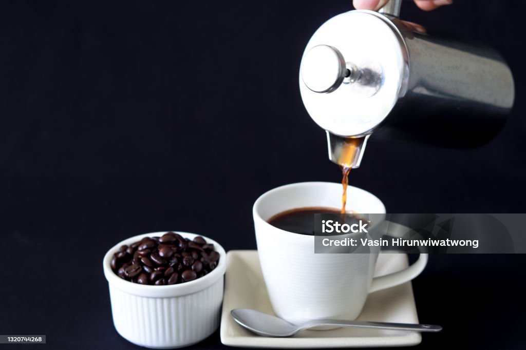 Pouring coffee from French Press coffee maker Pouring coffee from French Press coffee maker, into a cup on black background. There is coffee beans at side of coffee cup. French Press Stock Photo