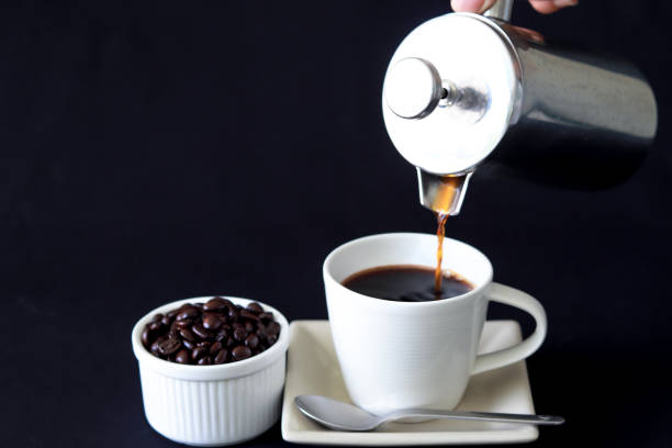 Pouring coffee from French Press coffee maker Pouring coffee from French Press coffee maker, into a cup on black background. There is coffee beans at side of coffee cup. glass cup of boiling water stock pictures, royalty-free photos & images