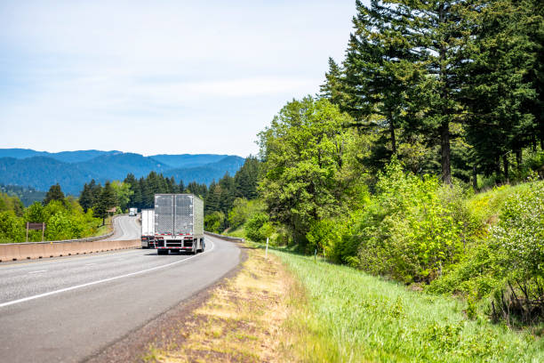 istock Big rigs semi trucks with different semi trailers transporting cargo moving on the winding divided highway road at same directions 1320745234
