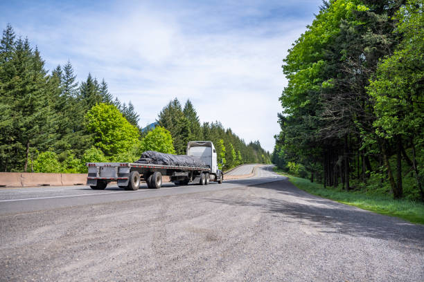 istock White industrial grade big rig semi truck transporting covered cargo on flat bed semi trailer running on the curving road in Columbia Gorge 1320745916