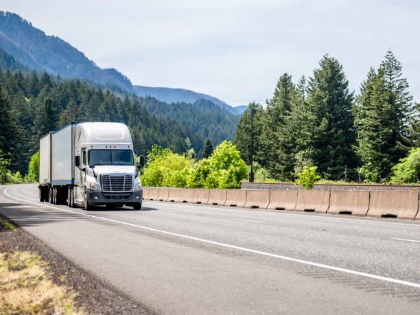 istock White bonnet big rig semi truck transporting cargo in two dry van semi trailers climbing on the winding mountain road with green forest around 1320748107