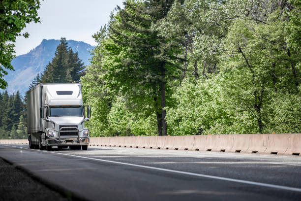 istock White powerful big rig semi truck with pipe grille guard transporting cargo in dry van semi trailer driving on the multiline highway green road 1320748240