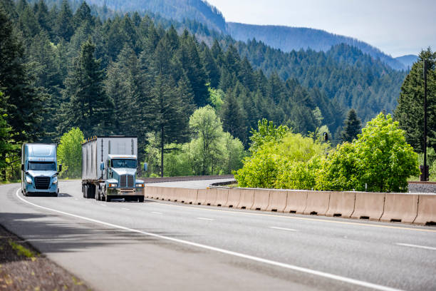 istock Two different big rig semi trucks with semi trailers running side by side on the winding multiline highway road with mountain and forest in Columbia Gorge 1320749280
