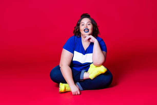 Happy plus size model in casual clothes, fat woman in blue jeans, t-shirt and yellow sneakers on red background Happy plus size model in casual clothes, fat woman in blue jeans, t-shirt and yellow sneakers on red background, body positive concept plus size woman fashion laughing stock pictures, royalty-free photos & images