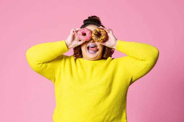 istock Cheerful plus size model holding donuts against her eyes on pink background 1320750260