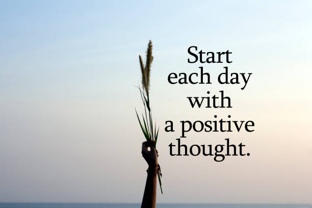 Start each day with a positie thought. With person holding flower plant in hand on blue sky background. Inspirational quote - Start each day with a positive thought. With arm of young woman raised holding grass flower plant in hand against soft color of sunset sky. Hope and positive thinking concept. monday stock pictures, royalty-free photos & images