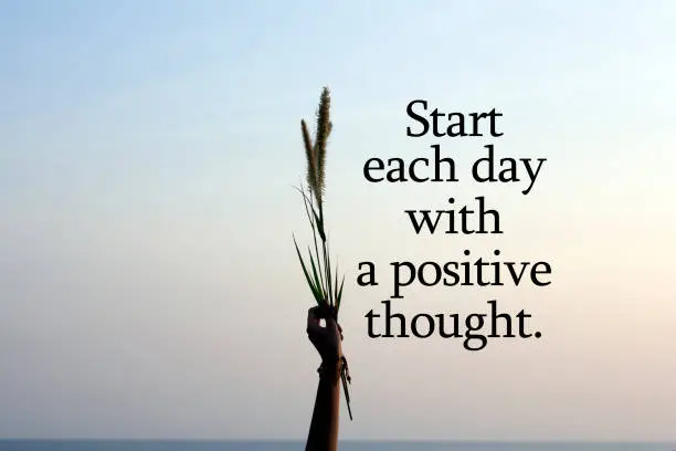Photo of Start each day with a positie thought. With person holding flower plant in hand on blue sky background.