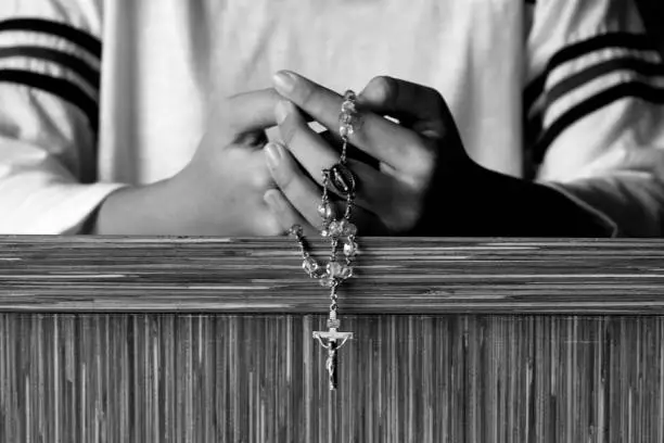 Photo of Person Kneel and Praying Rosary in black and white.